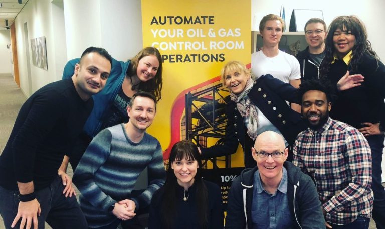 A photo of Vicki Knott and the rest of the CRUX OCM team posing in front of a promotional banner